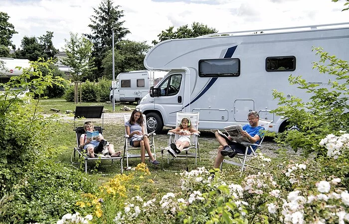 Familie mit zwei Kindern in Liegestühlen vor dem Wohnmobil