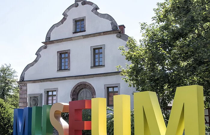 Weißes Haus in Giebelansicht mit bunten Lettern zum Museum