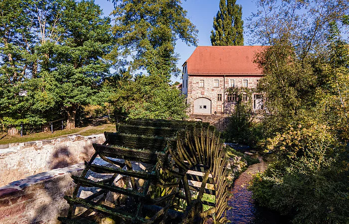 Wasserrad im Vordergrund am Bach und Haus im Hintergrund