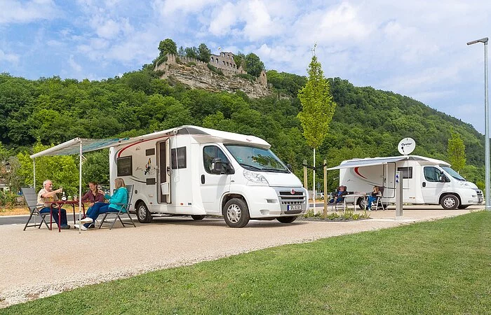 Wohnmobile am Platz mit sitzender Personengruppe davor, im Hintergrund Karlburg