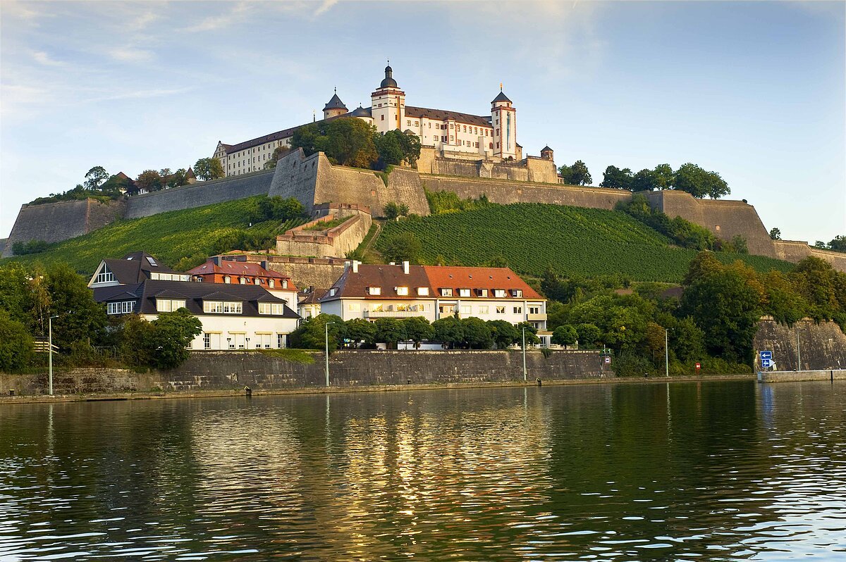 Burganlage der Festung auf der Anhöhe, von der Ferne mit Bastionen und Weinbergen, davor der Main
