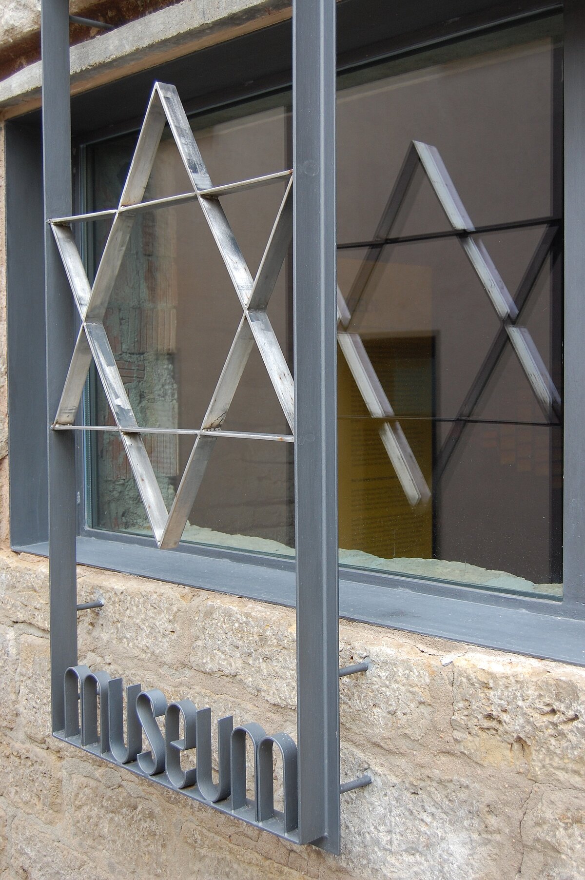 Sechszackiger Stern - Davidstern -  aus Metall im Metallrahmen, Schrift am unteren Ende - Museum
