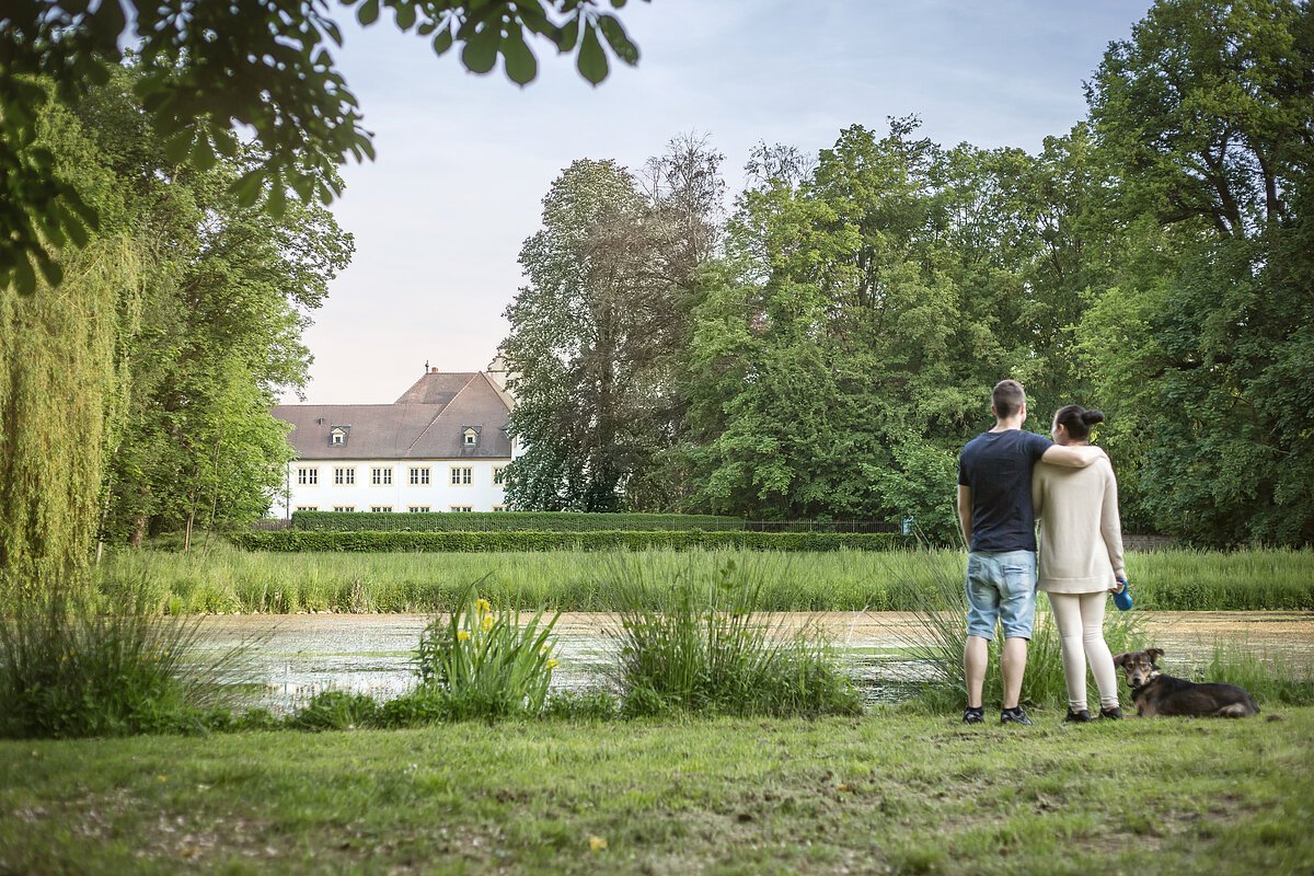 Anlage mit See und einem Pärchen, im Hintergrund längliches Haus